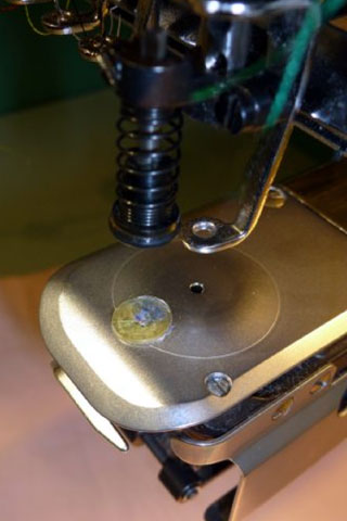 The stitch plate has a flexible plate in the front part that covers a hole. A spring-loaded punch with the bore needle inside holds the fabric during the cutting process